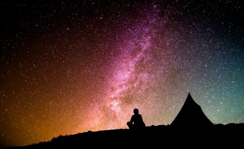 Mann sitzt vor Zelt und schaut in den Nachthimmel